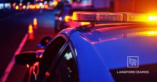 A police car at night alongside a road with emergency lights flashing.
